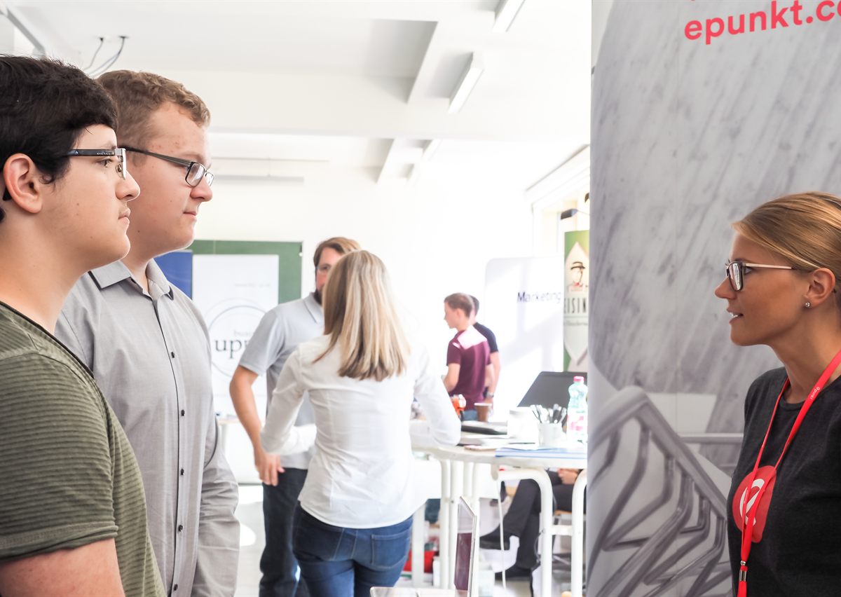Zwei Schüler im Gespräch mit einer Firmenvertreterin an einem Messestand