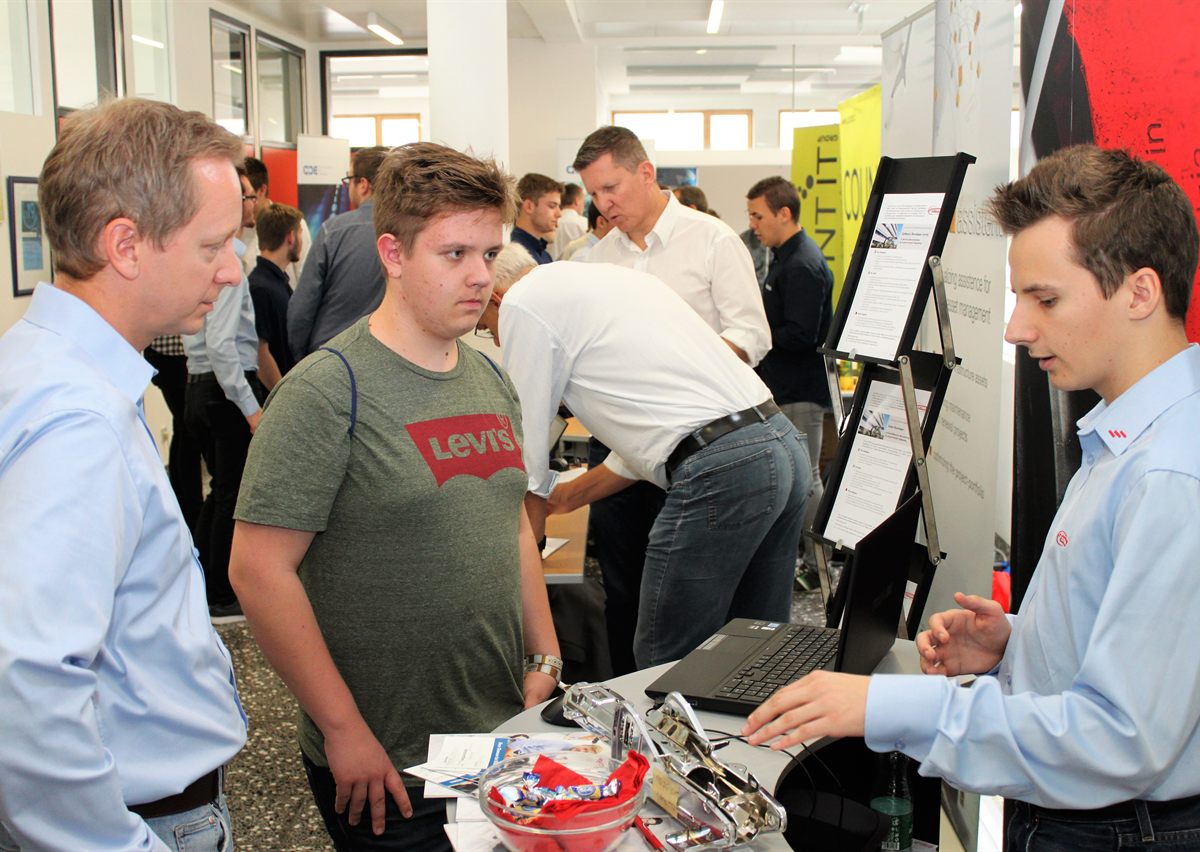 Firmenvertreter erklärt einem Schüler am Stand ein Projekt am Laptop