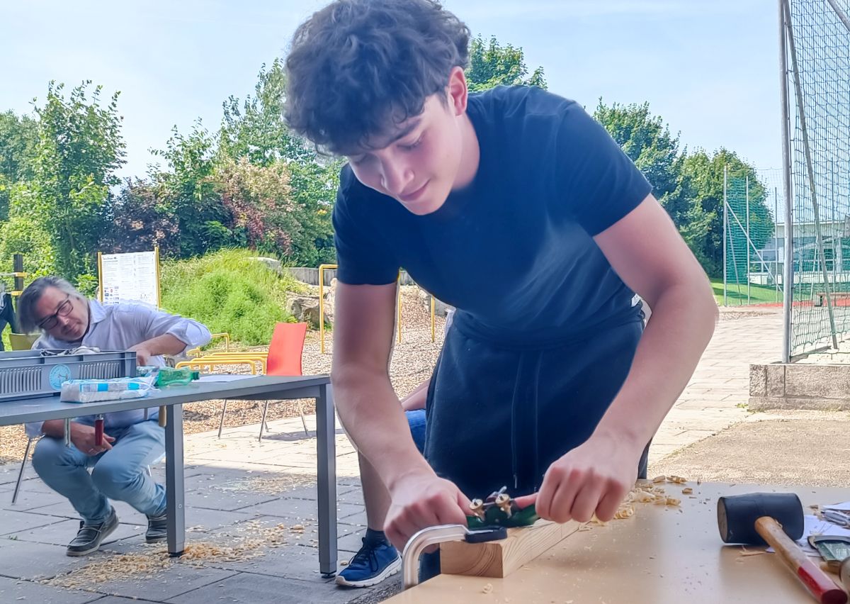 Schüler hobelt im Freien ein Holzteil für ein Windrad-Projekt