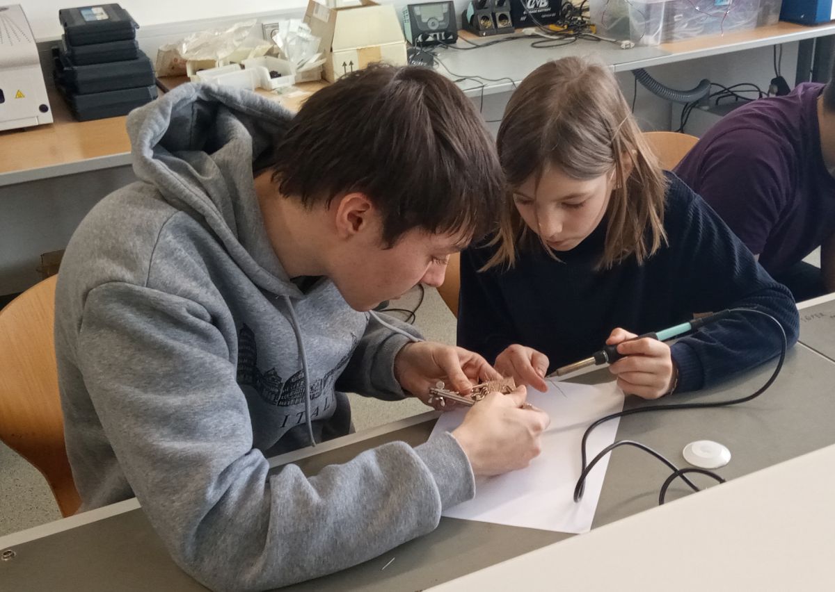 Volksschülerin lötet eine Platine, ein HTL-Schüler hilft ihr dabei